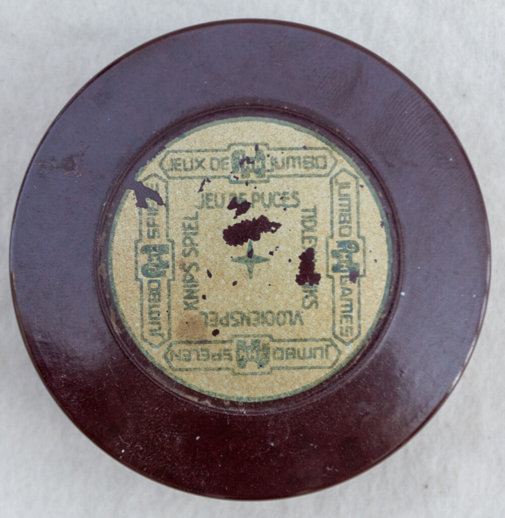 Tucker Tw ID • JUM-15c1 — AGPI ID • G-38386c1 — publisher • Jumbo Games; Jeux de Jumbo; Jumb — title • JEU DE PUCES • TIDLEYWINKS • VLOOIENSPEL • KNIPS SPIEL — notes • Bakelite cylinder with screwtop.