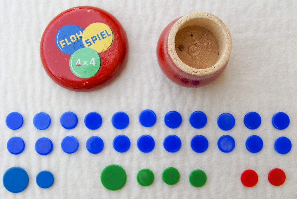 Tucker Tw ID • UNK-167c1 — AGPI ID • G-38355c1 — publisher • (unknown, German) — title • FLOH SPIEL 4x4 — notes • Red wooden mushroom container. "FLOH" on blue wink, "SPIEL" on yellow wink, "4x4" on green wink.